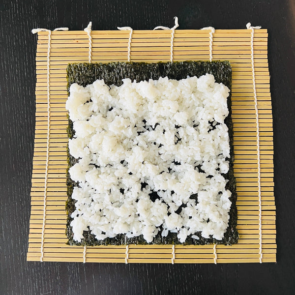 placing the rice covered nori seaweed sheet onto a bamboo rolling mat