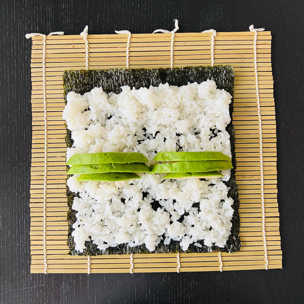 placing the sliced avocado in the middle of the rice covered nori seaweed sheet