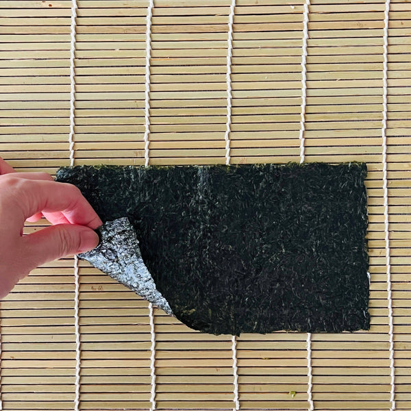 placing the nori seaweed shiny side down onto the bamboo rolling mat