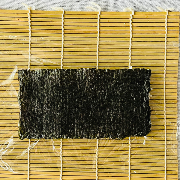 placing the rice covered nori seaweed onto a piece of plastic wrap shiny side up