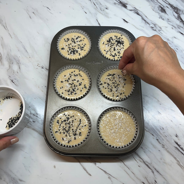 topping the mochi muffins with sesame seeds and shredded coconut