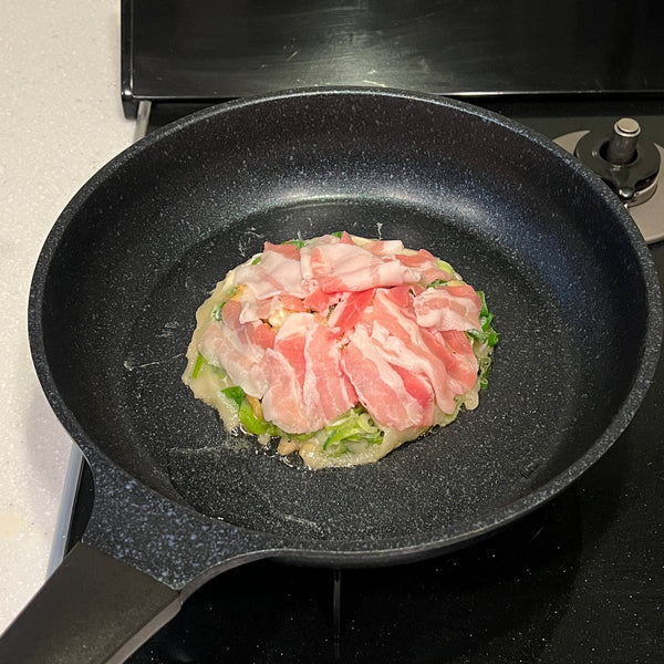 adding the sliced pork belly on top of the negiyaki