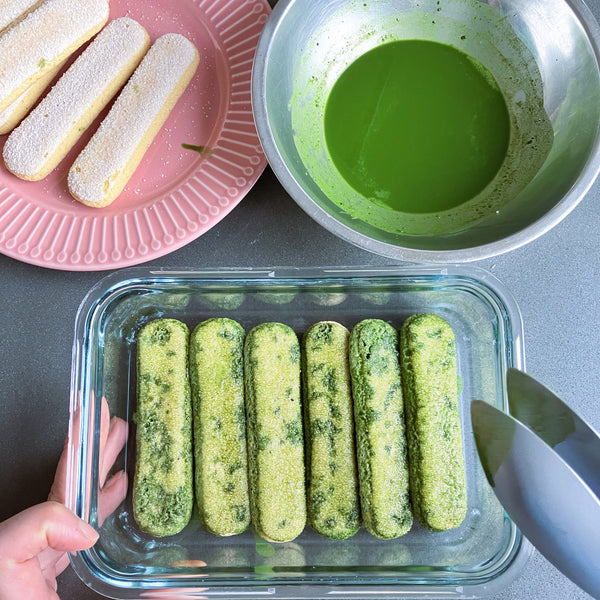 laying down a single layer of matcha-soaked ladyfingers into the container
