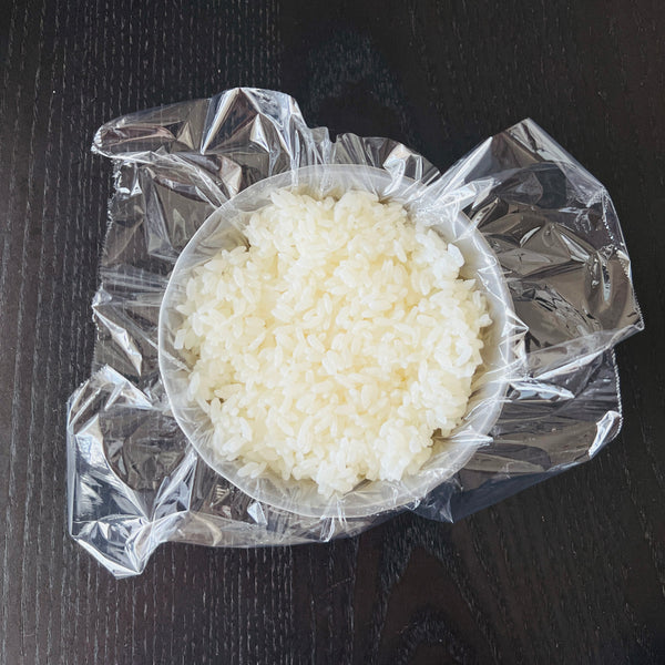 adding hot steamed rice into the plastic-wrapped bowl