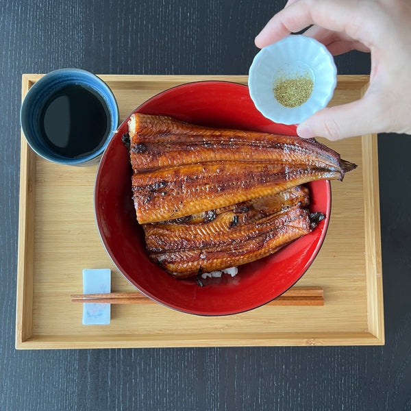 placing unagi over a bowl of rice and topping with sansho